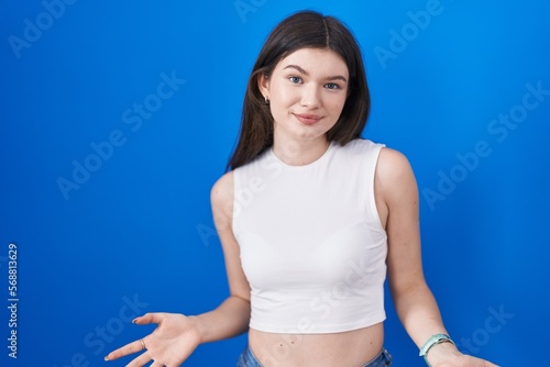Young caucasian woman standing over blue background smiling cheerful with open arms as friendly welcome  positive and confident greetings