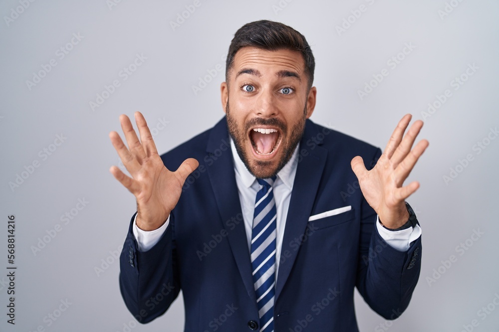 Handsome hispanic man wearing suit and tie celebrating crazy and amazed for success with arms raised and open eyes screaming excited. winner concept Handsome hispanic man wearing suit and tie celebrating crazy and amazed for success with arms raised and open eyes screaming excited. winner concept