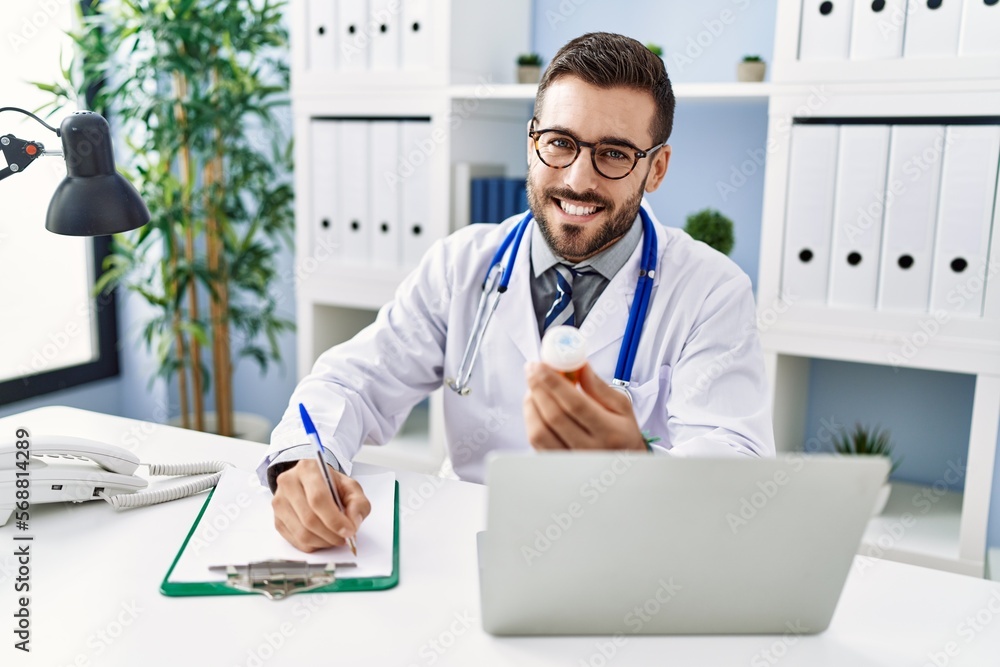 Young hispanic man wearing doctor uniform prescribing pills at clinic Young hispanic man wearing doctor uniform prescribing pills at clinic