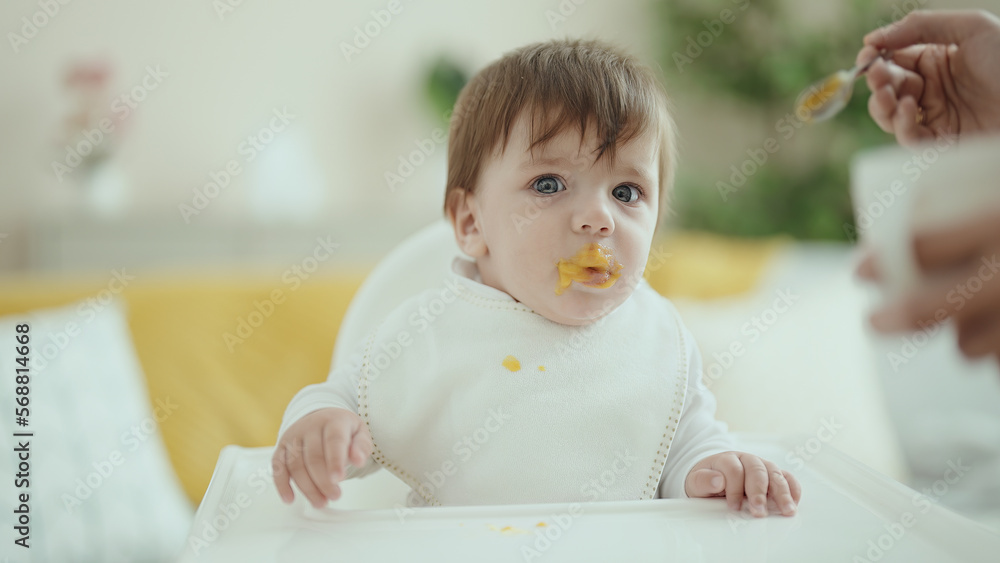 Adorable hispanic toddler sitting on highchair eating food at home Adorable hispanic toddler sitting on highchair eating food at home