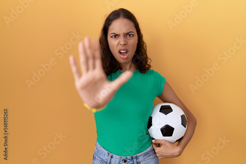 Young hispanic woman holding ball doing stop gesture with hands palms, angry and frustration expression © Krakenimages.com