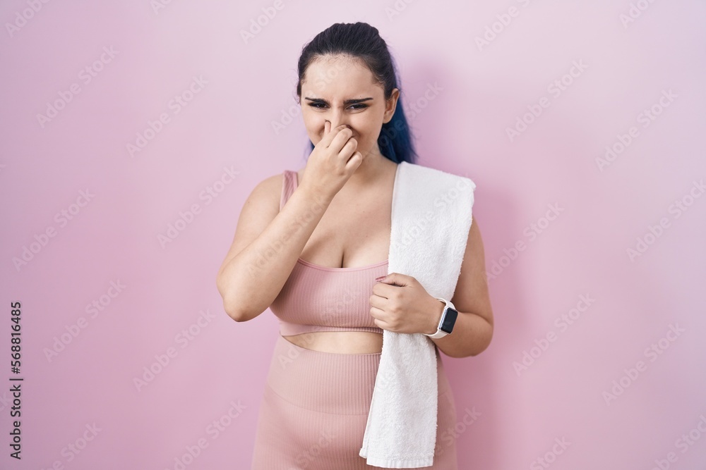 Young modern girl with blue hair wearing sportswear over pink background smelling something stinky and disgusting, intolerable smell, holding breath with fingers on nose. bad smell Young modern girl with blue hair wearing sportswear over pink background smelling something stinky and disgusting, intolerable smell, holding breath with fingers on nose. bad smell