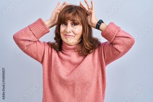 Middle age hispanic woman standing over isolated background doing bunny ears gesture with hands palms looking cynical and skeptical. easter rabbit concept.