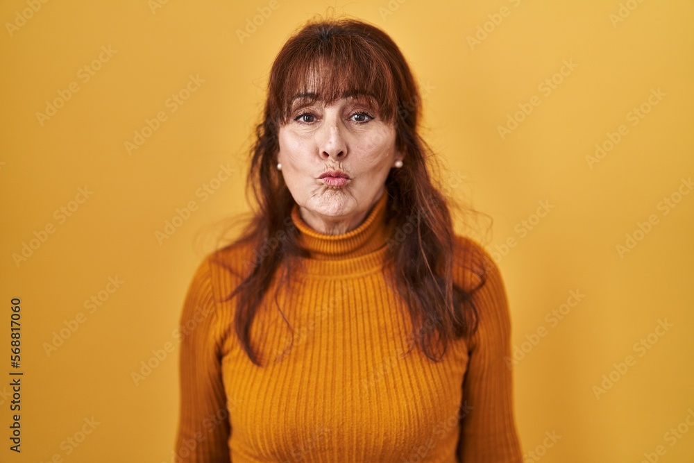 Middle age hispanic woman standing over yellow background looking at the camera blowing a kiss on air being lovely and sexy. love expression. Middle age hispanic woman standing over yellow background looking at the camera blowing a kiss on air being lovely and sexy. love expression.