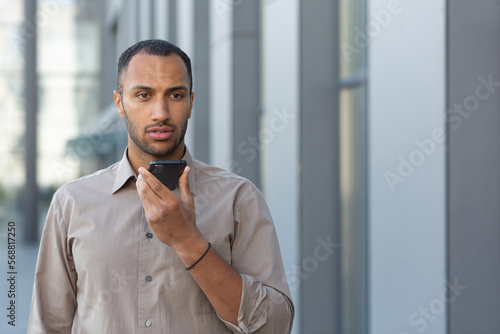 Wallpaper Mural Angry businessman in shirt recording audio message from outside office building, african american man using assistant giving commands to artificial intelligence using smartphone