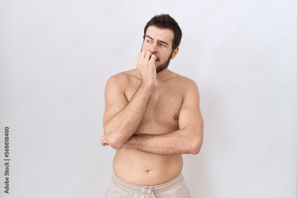 Young hispanic man standing shirtless over white background looking stressed and nervous with hands on mouth biting nails. anxiety problem.
