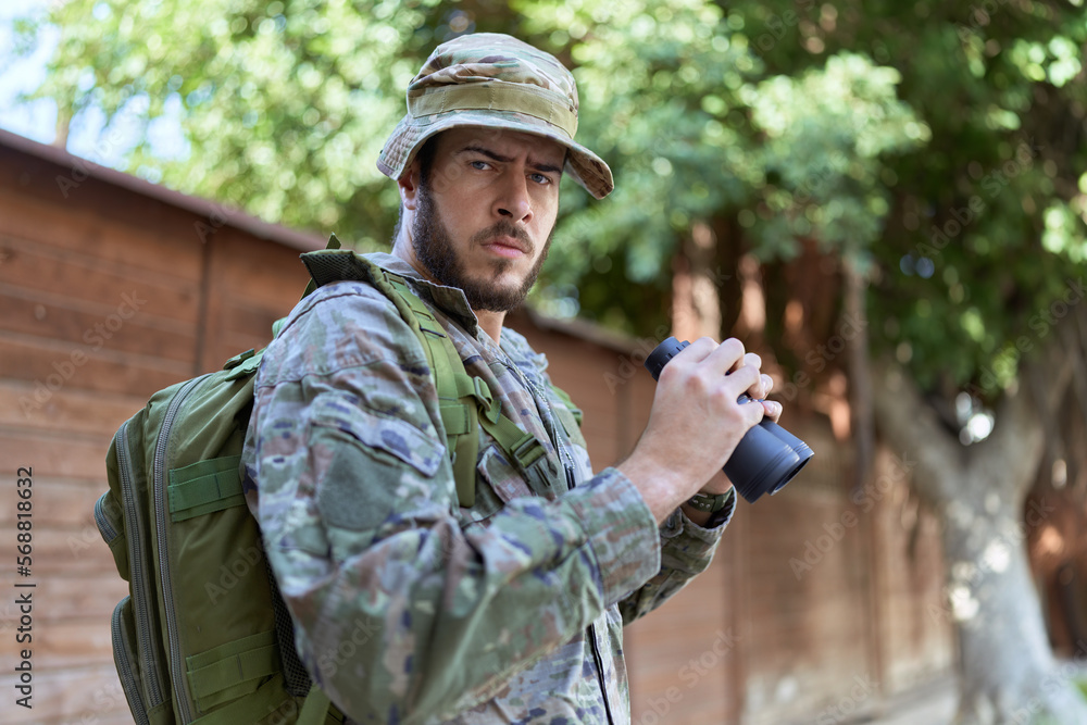 Young hispanic man wearing soldier uniform using binoculars at park