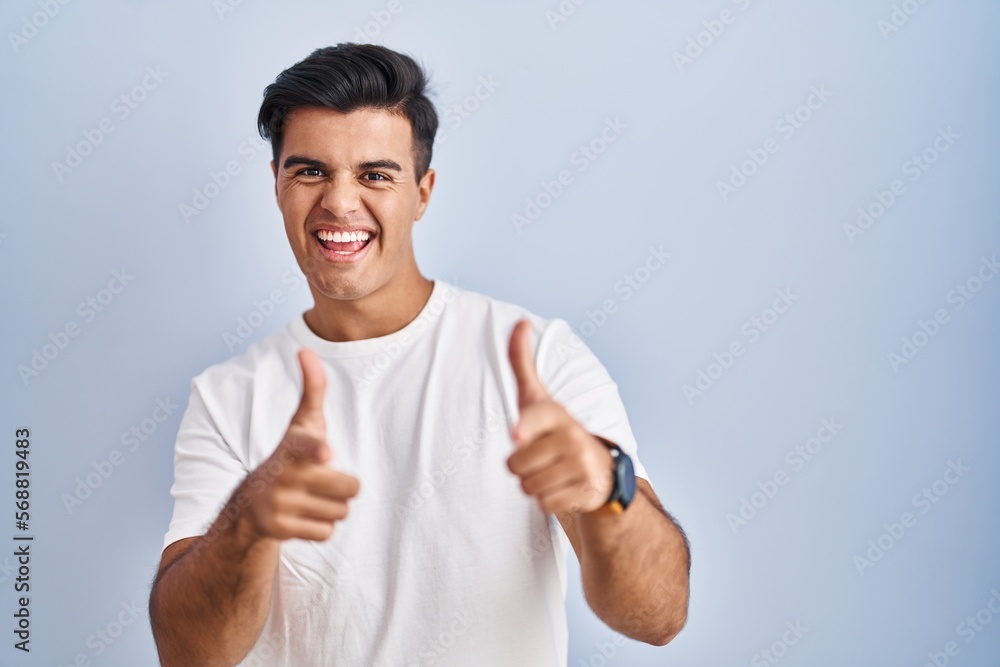 Hispanic man standing over blue background pointing fingers to camera with happy and funny face. good energy and vibes. Hispanic man standing over blue background pointing fingers to camera with happy and funny face. good energy and vibes.