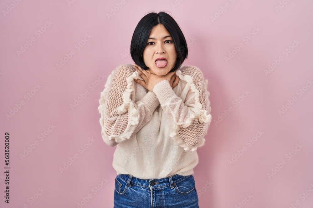 Young asian woman standing over pink background shouting and suffocate because painful strangle. health problem. asphyxiate and suicide concept. Young asian woman standing over pink background shouting and suffocate because painful strangle. health problem. asphyxiate and suicide concept.