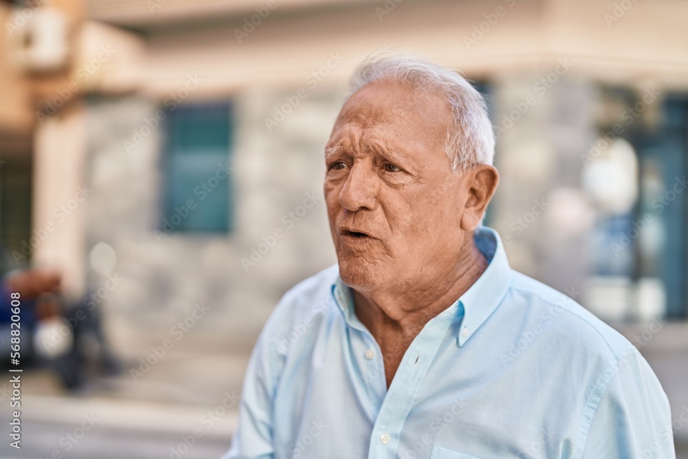 Senior grey-haired man with relaxed expression standing at street Senior grey-haired man with relaxed expression standing at street