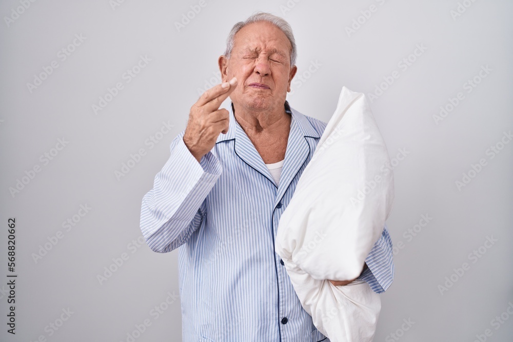 Senior man with grey hair wearing pijama hugging pillow gesturing finger crossed smiling with hope and eyes closed. luck and superstitious concept. Senior man with grey hair wearing pijama hugging pillow gesturing finger crossed smiling with hope and eyes closed. luck and superstitious concept.
