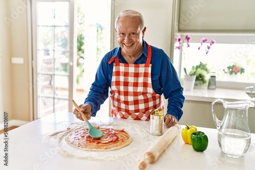 Senior man smiling confident cooking pizza at kitchen