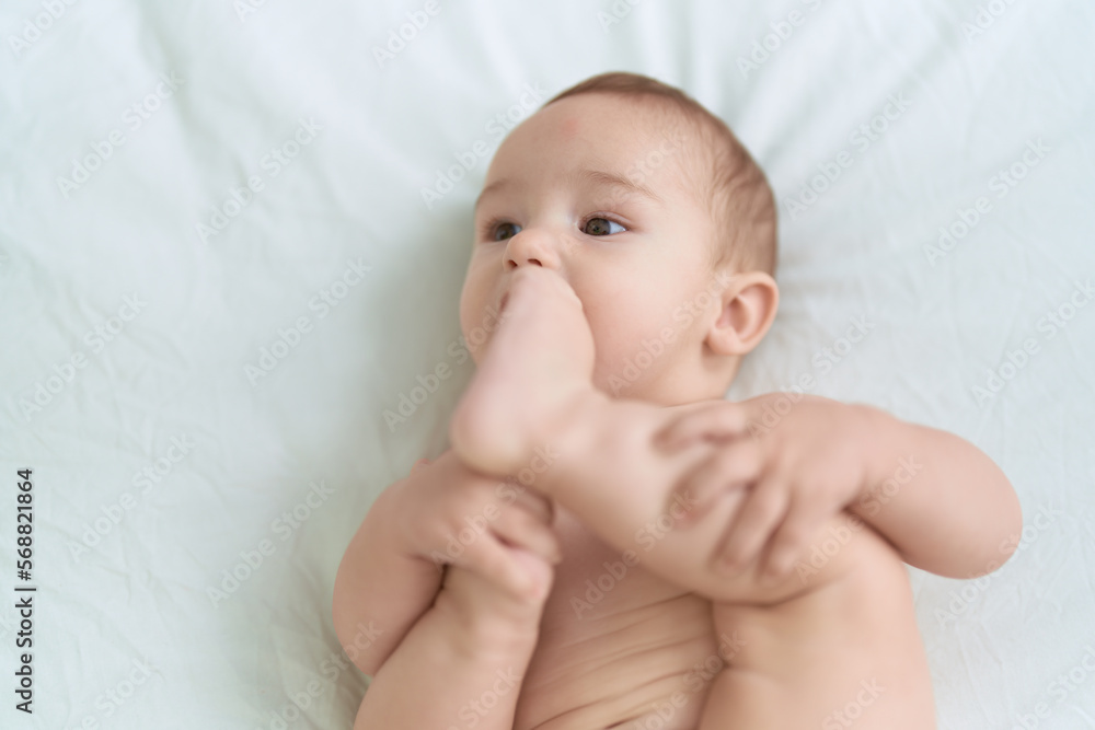 Adorable toddler lying on bed sucking feet at bedroom Adorable toddler lying on bed sucking feet at bedroom