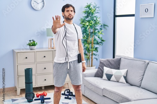 Handsome latin man wearing sportswear at home doing stop sing with palm of the hand. warning expression with negative and serious gesture on the face.