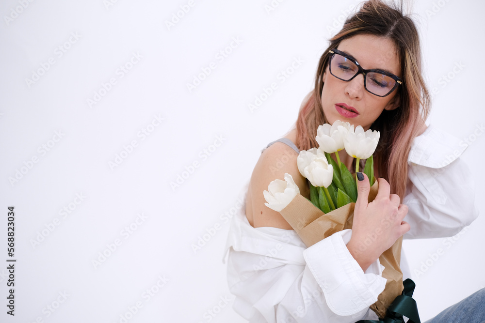 Woman in white shirt sitting and hugging a bouquet of white tulips on a white background. Feminine. White shirt. Gift concept for woman, love, birthday, 8 March, mother day. Copy space. Woman in white shirt sitting and hugging a bouquet of white tulips on a white background. Feminine. White shirt. Gift concept for woman, love, birthday, 8 March, mother day. Copy space.