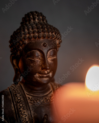 Close-up of the statue of Buddha with selective focus and blurred candlelight in the foreground. Buddhism concept