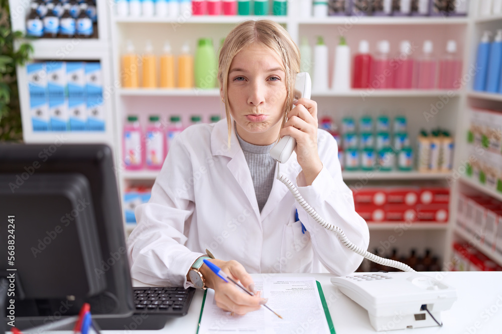 Young caucasian woman working at pharmacy drugstore speaking on the telephone depressed and worry for distress, crying angry and afraid. sad expression. Young caucasian woman working at pharmacy drugstore speaking on the telephone depressed and worry for distress, crying angry and afraid. sad expression.