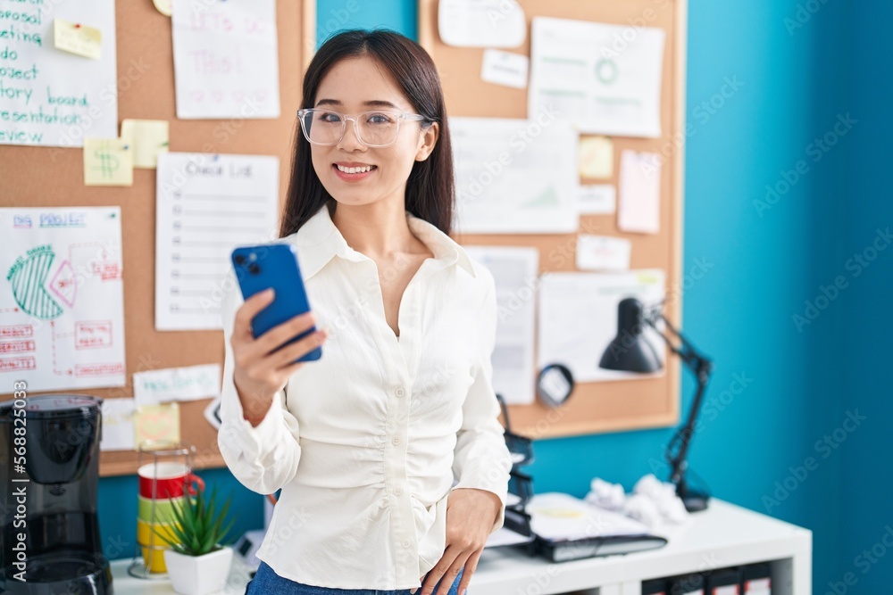Young chinese woman business worker smiling confident using smartphone at office
