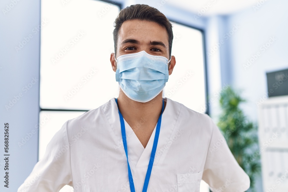Young hispanic man wearing physiotherapist uniform and medical mask at clinic Young hispanic man wearing physiotherapist uniform and medical mask at clinic