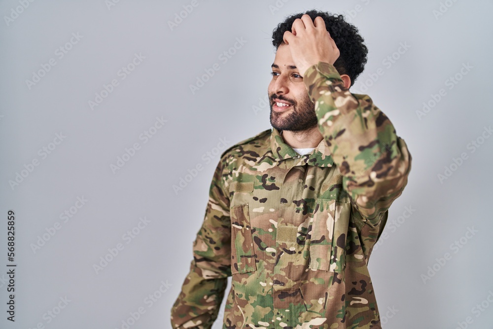 Arab man wearing camouflage army uniform smiling confident touching hair with hand up gesture, posing attractive and fashionable
