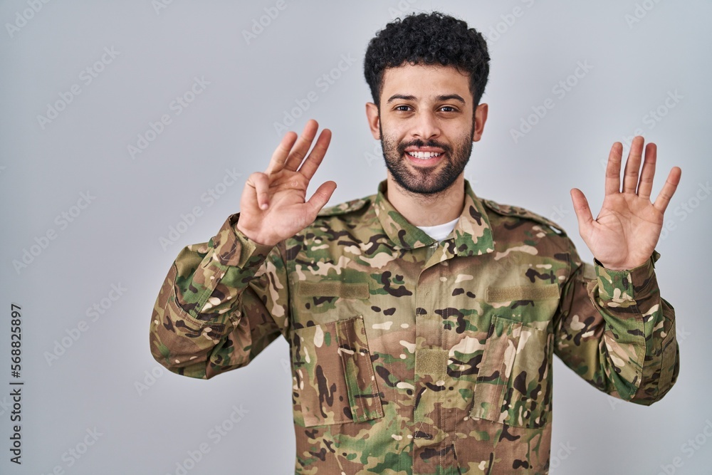 Arab man wearing camouflage army uniform showing and pointing up with fingers number nine while smiling confident and happy.