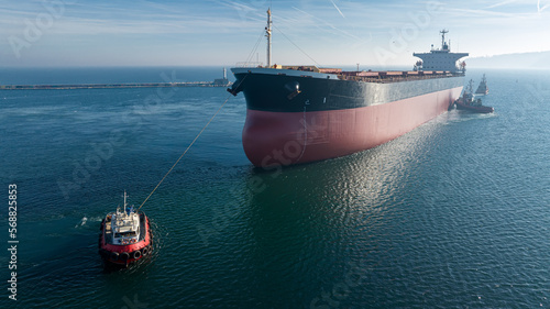 Aerial view of tug boat assisting big cargo ship. Large cargo ship enters the port escorted by tugboats. photo