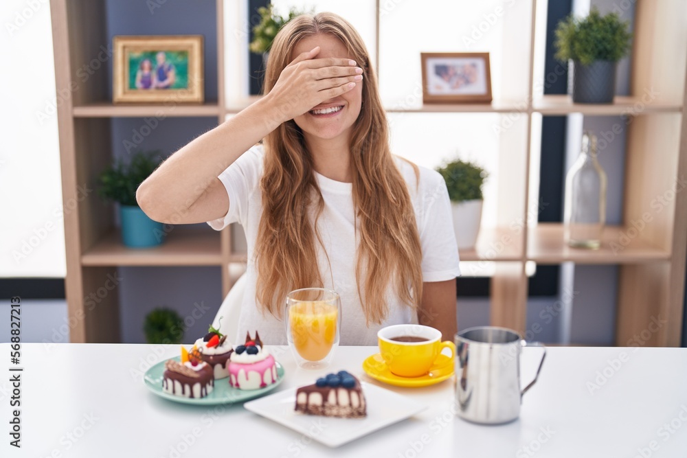 Young caucasian woman eating pastries t for breakfast smiling and laughing with hand on face covering eyes for surprise. blind concept.