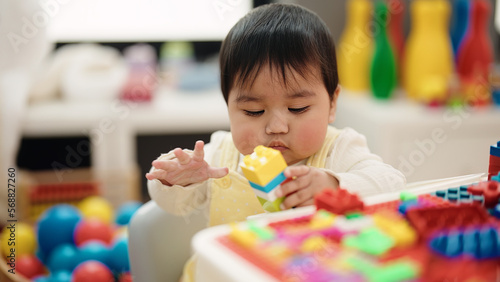 Adorable hispanic baby playing with construction blocks sitting on table at kindergarten