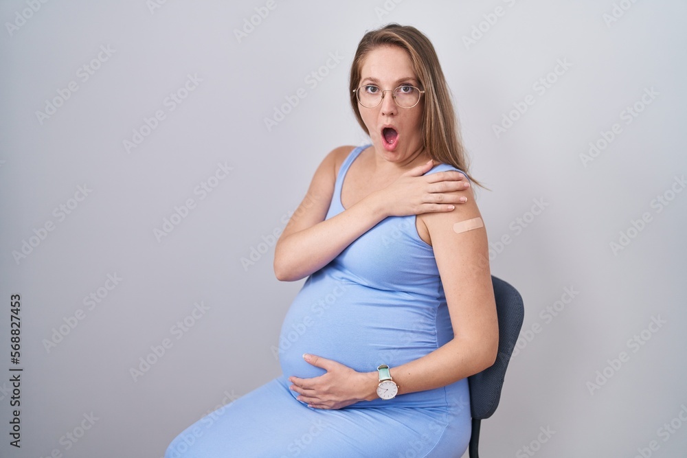 Young pregnant woman wearing band aid for vaccine injection scared and amazed with open mouth for surprise, disbelief face Young pregnant woman wearing band aid for vaccine injection scared and amazed with open mouth for surprise, disbelief face