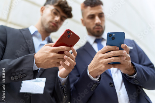 Two hispanic men business workers using smartphones at street