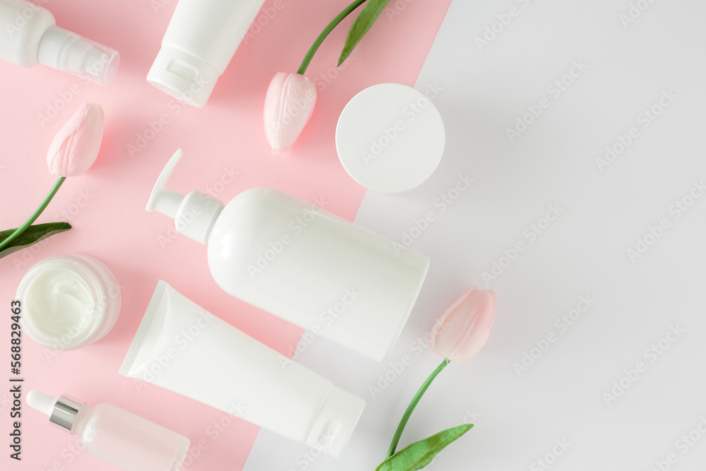 Organic cosmetic concept. Flat lay photo of cosmetic tubes without label, serum bottles, cream jars and spring flowers on pastel pink and white background. Cosmetic mockup. Organic cosmetic concept. Flat lay photo of cosmetic tubes without label, serum bottles, cream jars and spring flowers on pastel pink and white background. Cosmetic mockup.