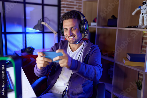 Young hispanic man streamer playing video game using smartphone at gaming room