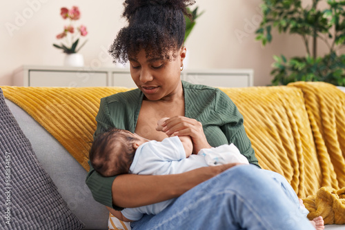 Фотография Mother and son sitting on sofa breastfeeding at home
