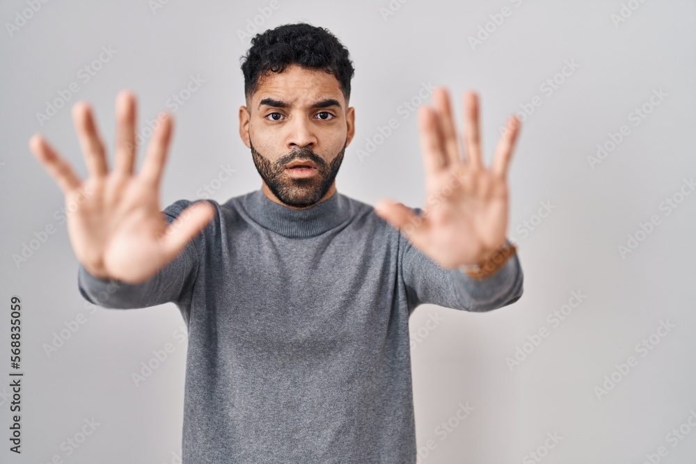 Hispanic man with beard standing over white background doing stop gesture with hands palms, angry and frustration expression Hispanic man with beard standing over white background doing stop gesture with hands palms, angry and frustration expression