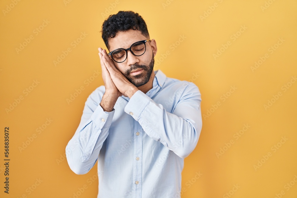 Hispanic man with beard standing over yellow background sleeping tired dreaming and posing with hands together while smiling with closed eyes. Hispanic man with beard standing over yellow background sleeping tired dreaming and posing with hands together while smiling with closed eyes.