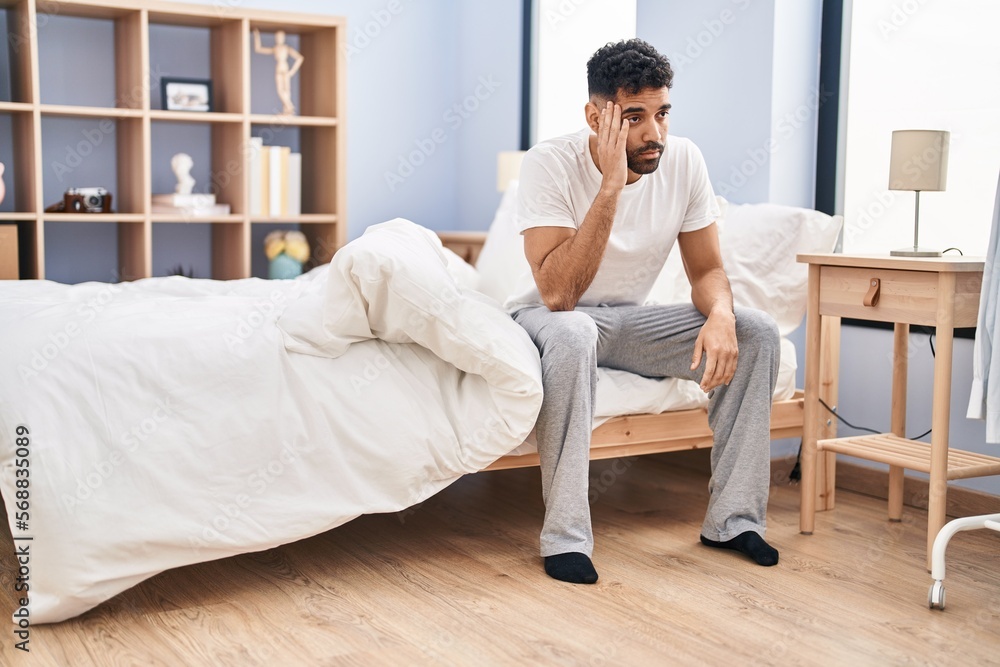 Young hispanic man suffering for headache sitting on bed at bedroom Young hispanic man suffering for headache sitting on bed at bedroom