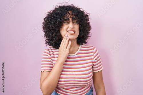 Young middle east woman standing over pink background touching mouth with hand with painful expression because of toothache or dental illness on teeth. dentist