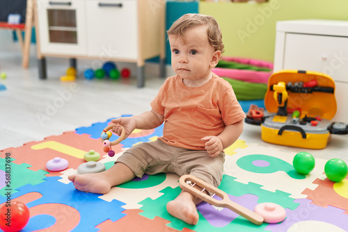 Adorable blond toddler playing with toys sitting on floor at kindergarten