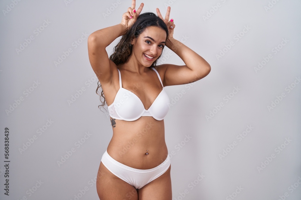 Young hispanic woman wearing white lingerie posing funny and crazy with fingers on head as bunny ears, smiling cheerful Young hispanic woman wearing white lingerie posing funny and crazy with fingers on head as bunny ears, smiling cheerful