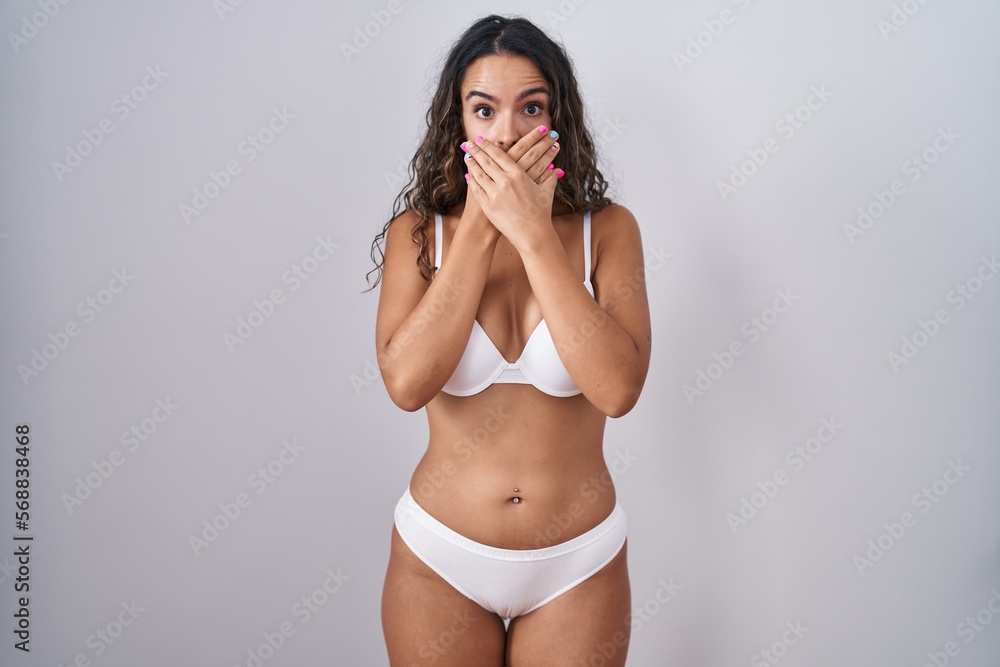 Young hispanic woman wearing white lingerie shocked covering mouth with hands for mistake. secret concept. Young hispanic woman wearing white lingerie shocked covering mouth with hands for mistake. secret concept.