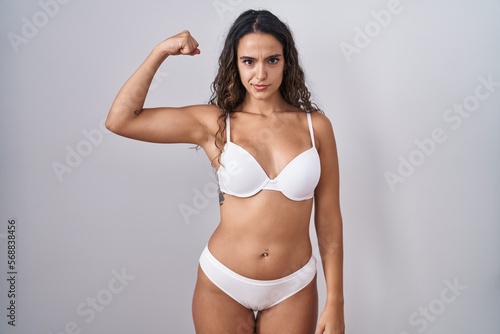 Young hispanic woman wearing white lingerie strong person showing arm muscle, confident and proud of power