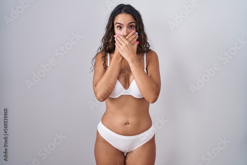 Young hispanic woman wearing white lingerie shocked covering mouth with hands for mistake. secret concept.