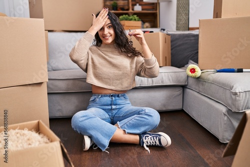 Young brunette woman sitting on the floor at new home holding keys stressed and frustrated with hand on head, surprised and angry face