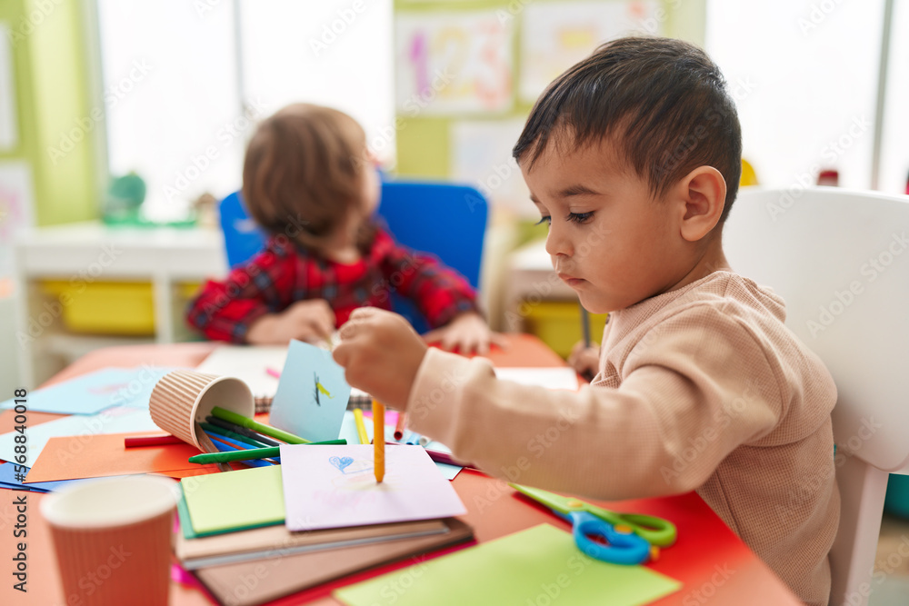 Fototapeta premium Two kids preschool students sitting on table drawing on paper at kindergarten
