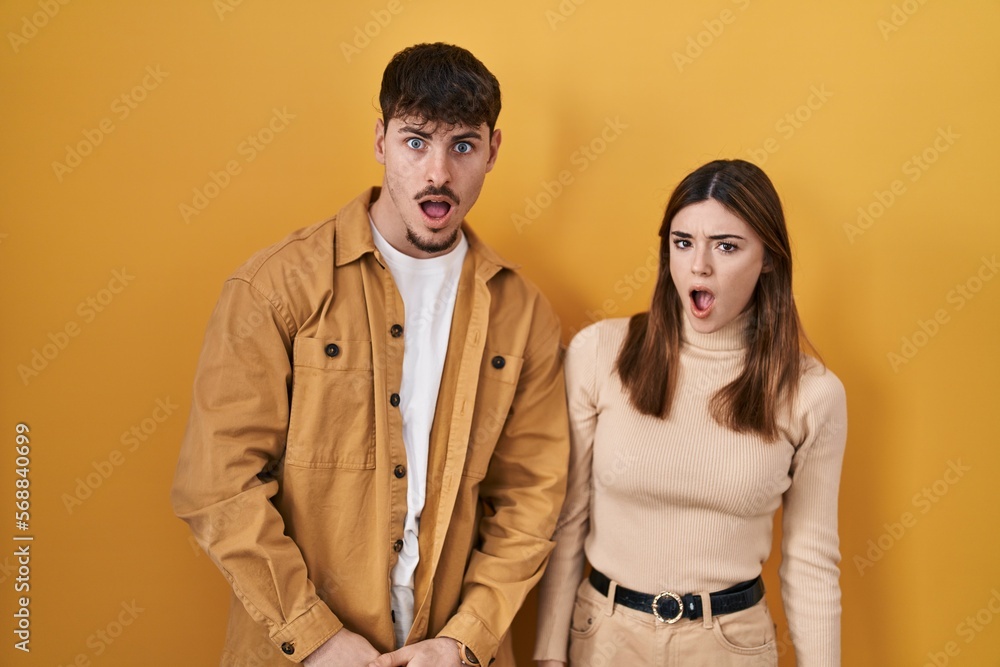 Young hispanic couple standing over yellow background in shock face, looking skeptical and sarcastic, surprised with open mouth Young hispanic couple standing over yellow background in shock face, looking skeptical and sarcastic, surprised with open mouth