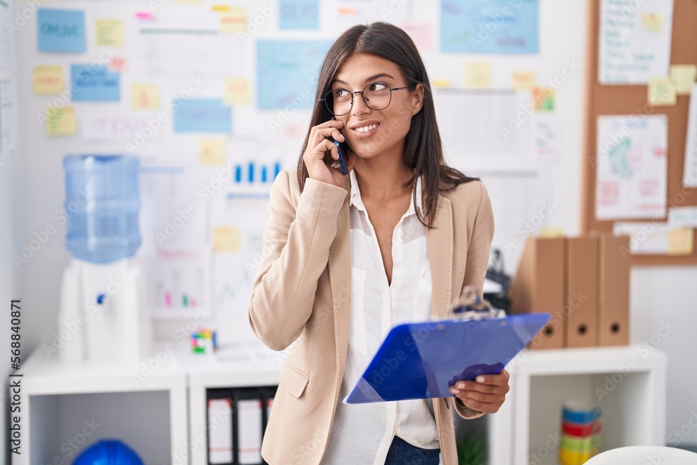 Young beautiful hispanic woman business worker talking on smartphone holding clipboard at office Young beautiful hispanic woman business worker talking on smartphone holding clipboard at office