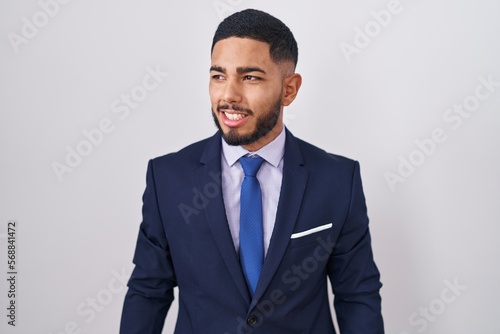 Young hispanic man wearing business suit and tie looking away to side with smile on face, natural expression. laughing confident.