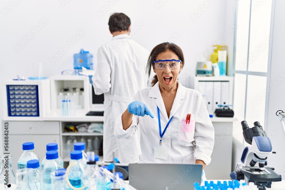 Middle age woman working at scientist laboratory smiling happy pointing with hand and finger