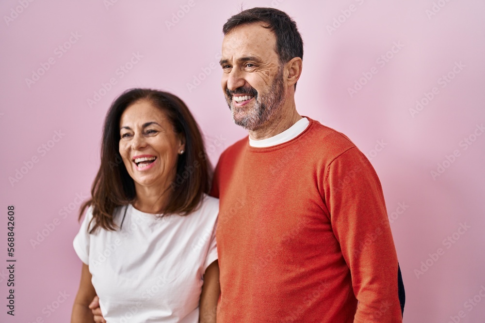 Fototapeta premium Middle age man and woman couple hugging each other standing over pink background