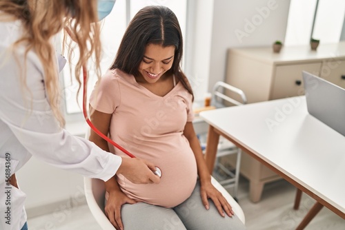 Young latin woman pregnant and doctor auscultating belly at clinic photo